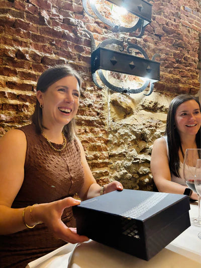 Two women sitting at a table with a black box in a rustic setting.