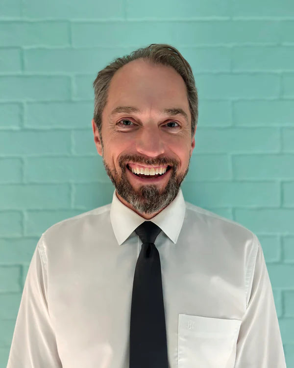 Man wearing a white shirt and black tie against a light blue brick wall