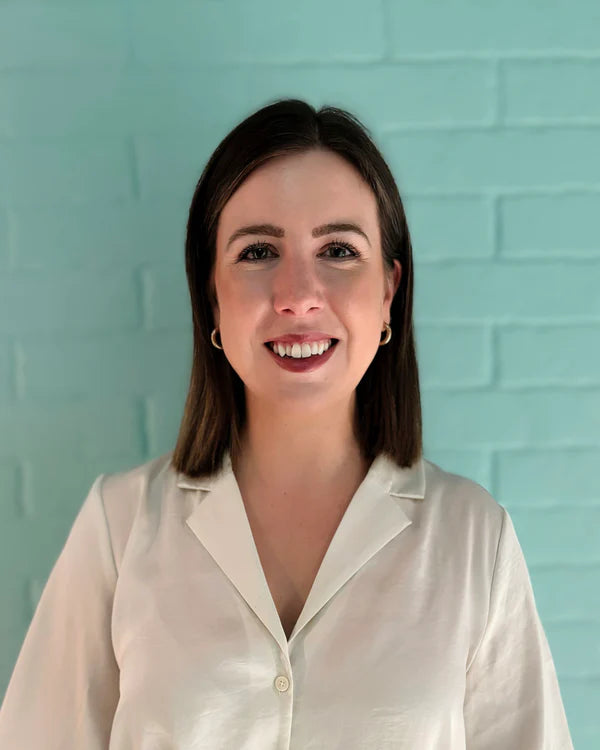 Woman wearing a white blouse against a light blue brick wall