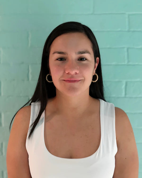 Woman wearing a white tank top against a light blue brick wall